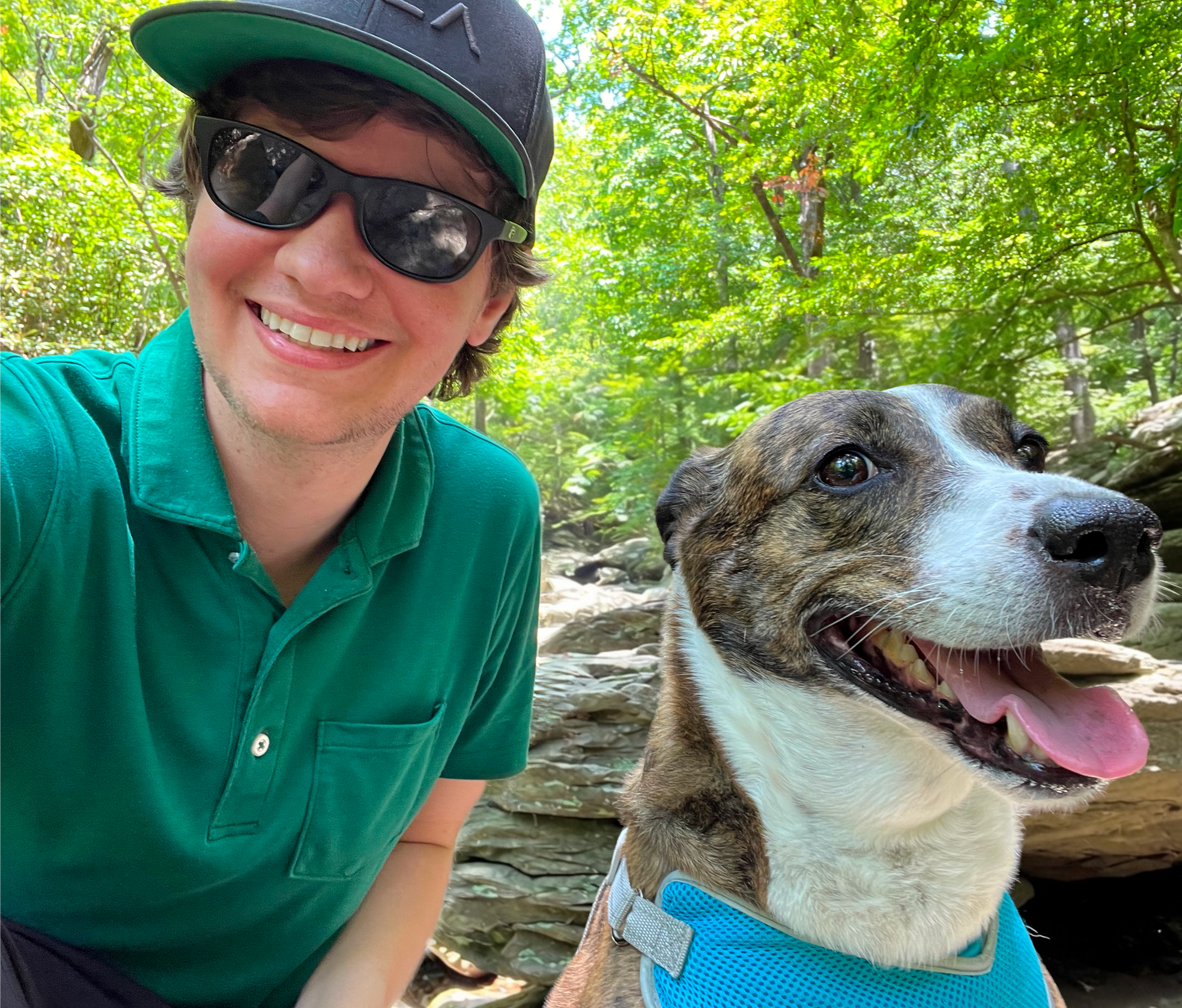 Jared with his dog Brindle in an outdoor wooded setting with boulders